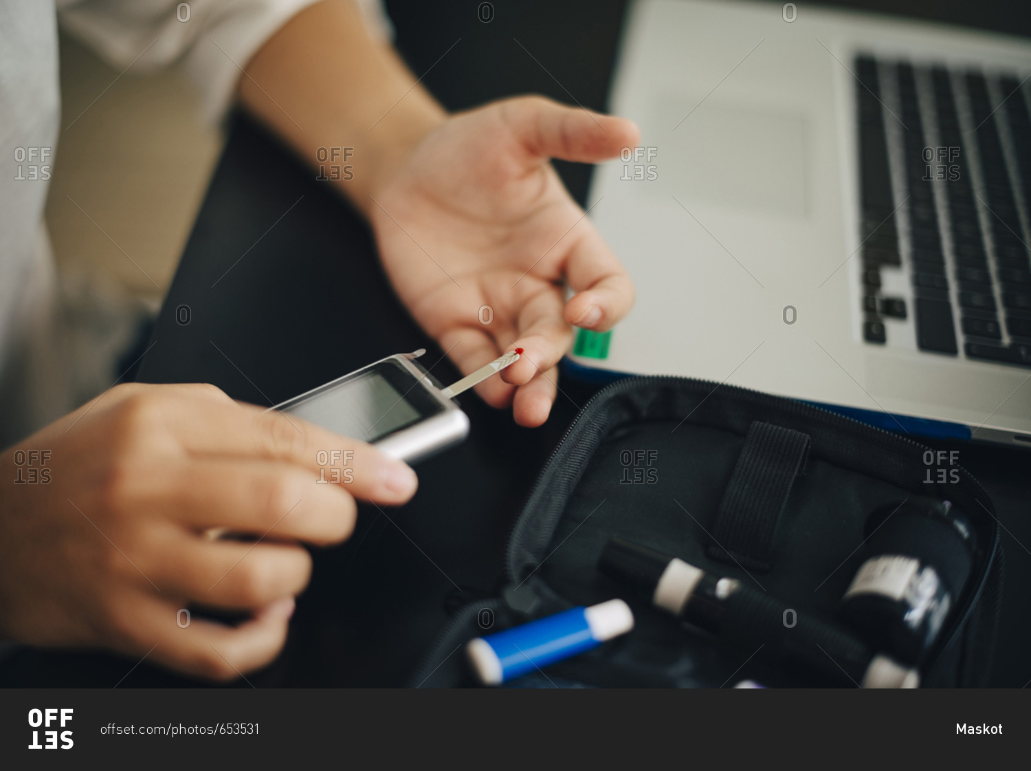 Cropped hands of businesswoman checking blood sugar level with glaucometer at desk
