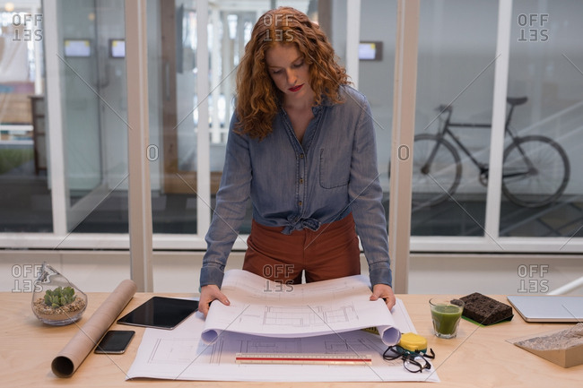 Female graphic designer working on blueprint in office stock photo - OFFSET