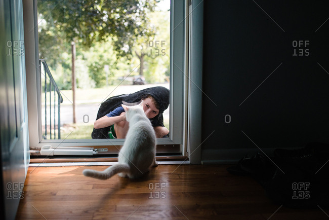 Boy playing with white cat through glass door