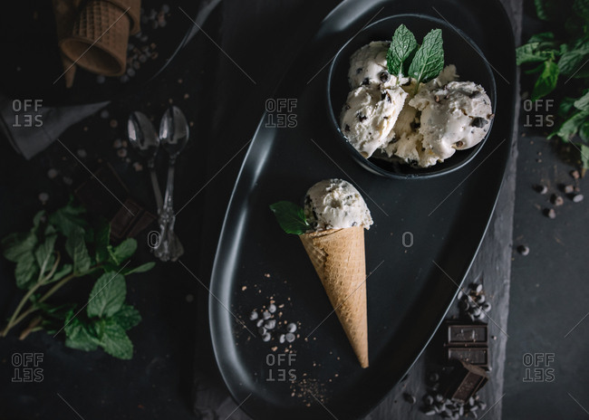 Overhead view of homemade chocolate chip ice cream in a cone and bowl garnished with mint leaves