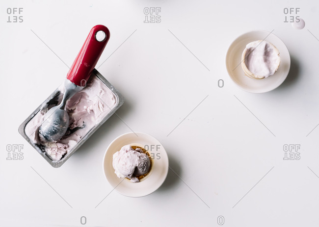 Overhead view of scoop in tub of homemade ice cream and ice cream cones in bowls