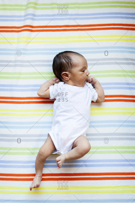 Tiny newborn lying awake on colorful bedsheet