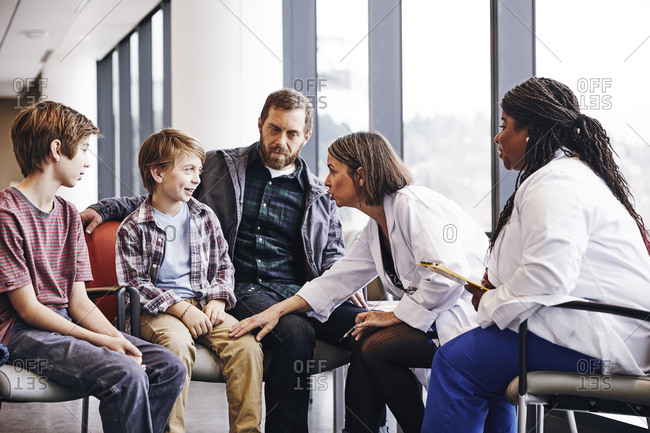 Female doctors talking to father and sons in hospital waiting room