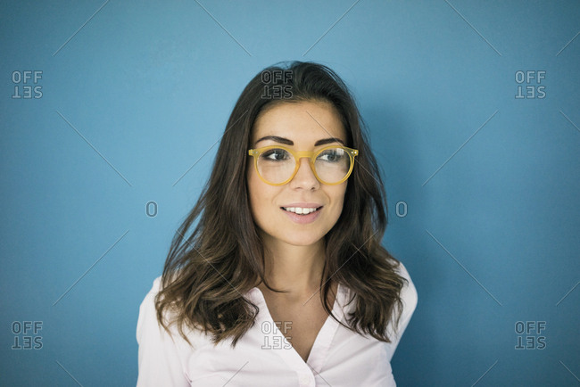 Portrait of smiling woman wearing glasses in front of blue background