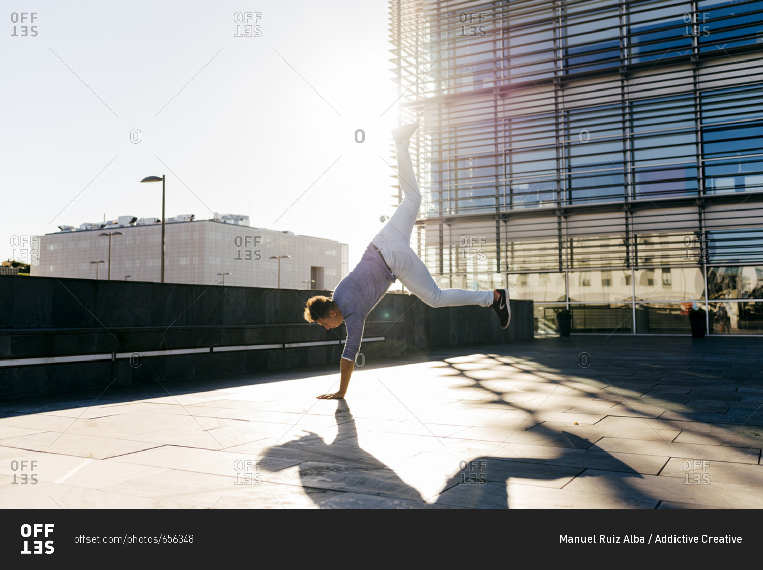 Side view of man standing on hand and performing trick in back lit on street