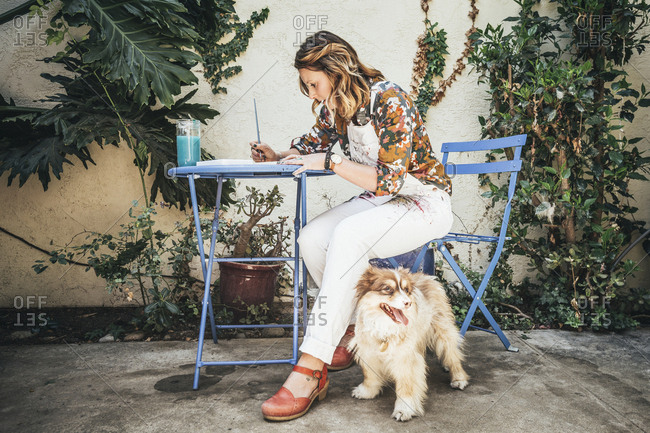 Full length of artist painting while sitting by dog on chair at backyard