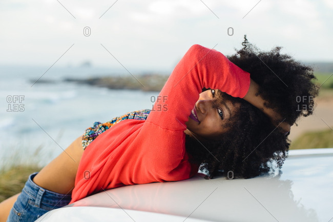 Happy stylish black woman relaxing towards the sea during car trip. Fashionable afro hair model on vacation to the coast.