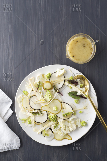 A salad of winter vegetables and fruits on a large plate with a serving spoon, a container of dressing, and a napkin.