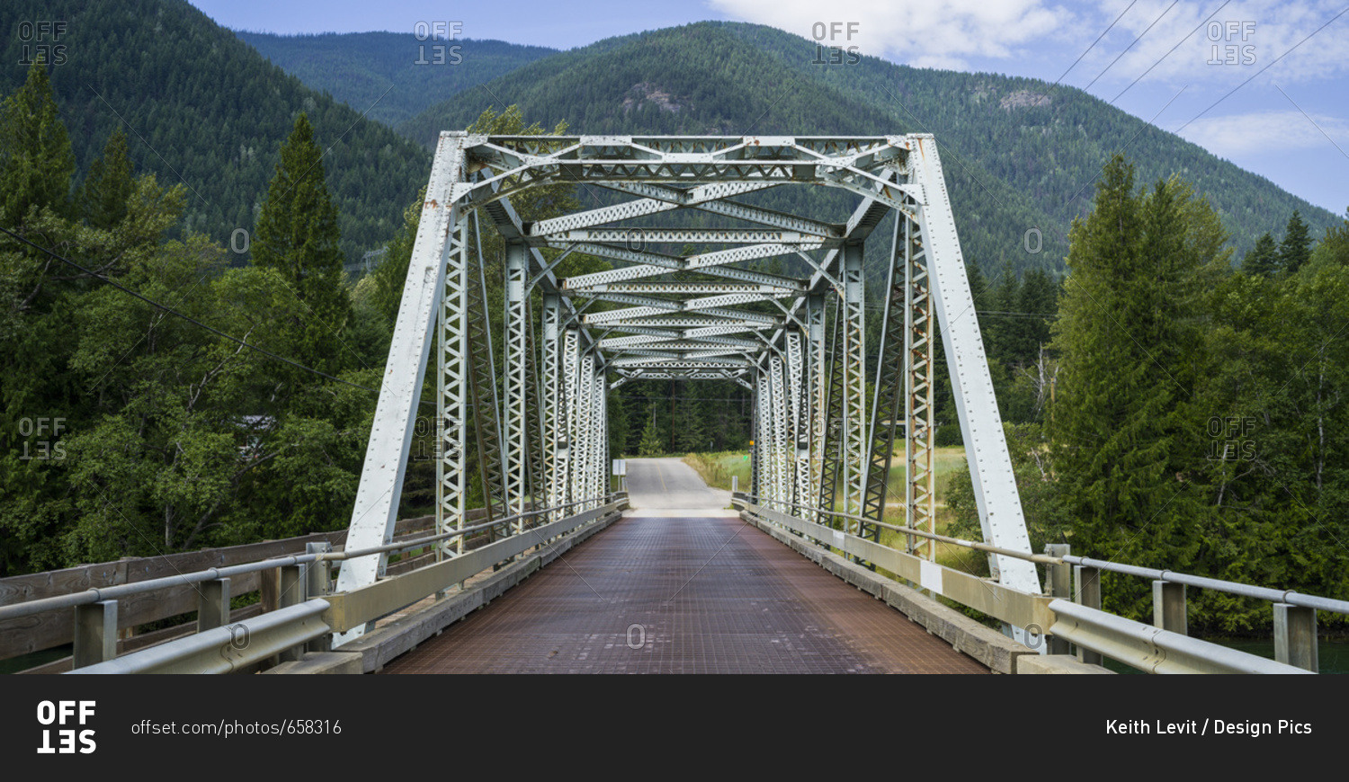 A road bridge over the Kootenay River with forests covering the Rocky mountains; British Columbia, Canada