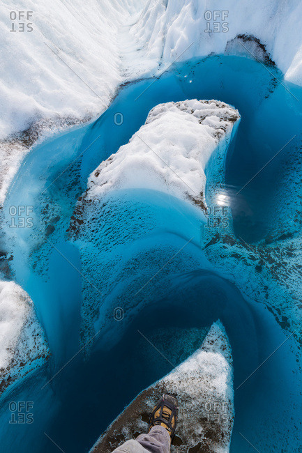A hiker's boot showing the point of view looking down into the deep, blue meltwater of a glacier in Wrangell-St. Elias National Park; Alaska, United States of America