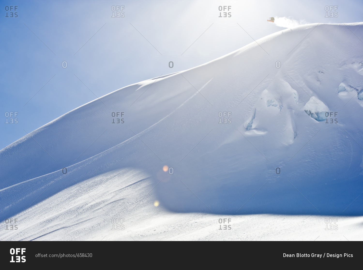 A professional, freeriding snowboarder in mid-air on a snowy slope against a blue sky; British Columbia, Canada