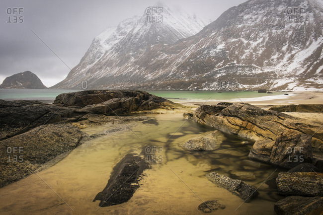 A landscape with rugged mountains and sand along the coastline under a cloudy sky; Nordland, Norway