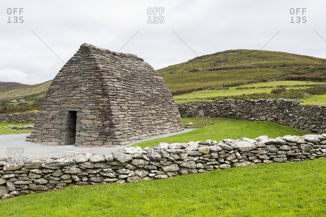 Beehive Stone Structure With Stone Fences And Grassy Hillside In The Background, Gallarus Oratory; Gallarus, County Kerry, Ireland