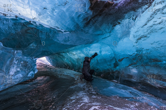 A Man Examines The Clear Blue Ice Inside A Tunnel Beneath The Surface Of Black Rapids Glacier In Winter; Alaska, United States Of America