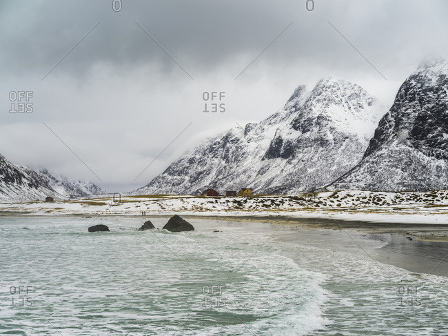 Landscape Of The Coastline And Rugged, Snow Covered Mountains Under A Cloudy Sky; Lofoten Islands, Nordland, Norway