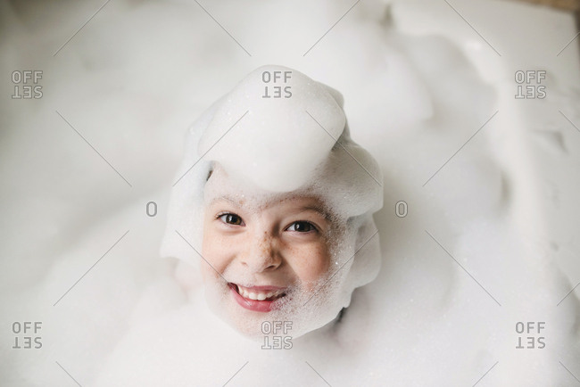 Happy kid covered in bubbles in a bubble bath