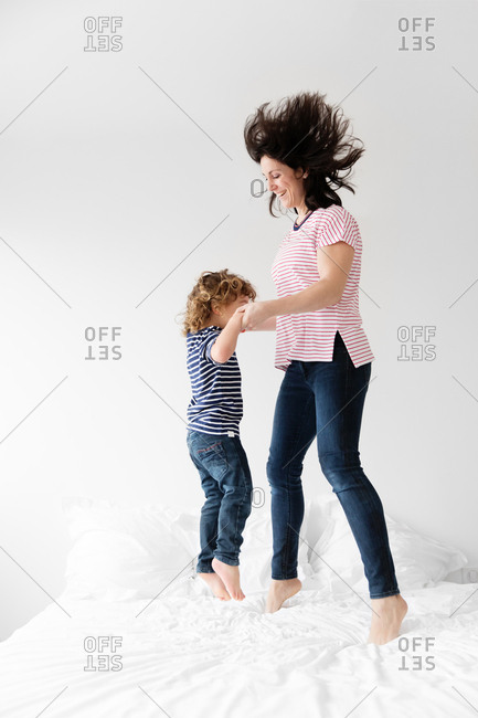 Mother And Young Son Jumping Up And Down On Bed Together Stock