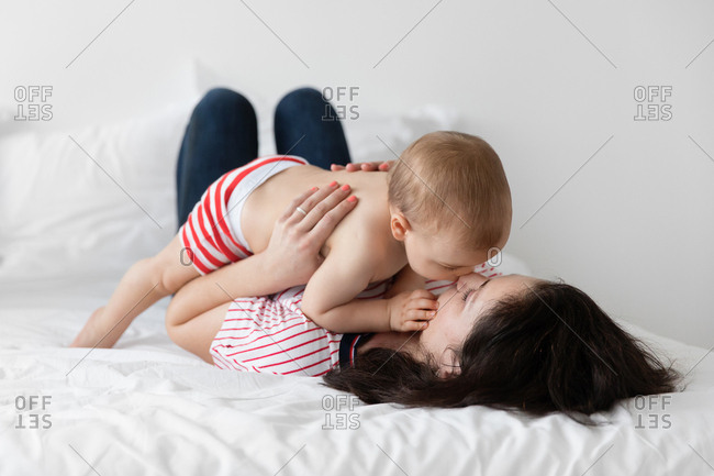 Mother nuzzling baby boy lying on bed
