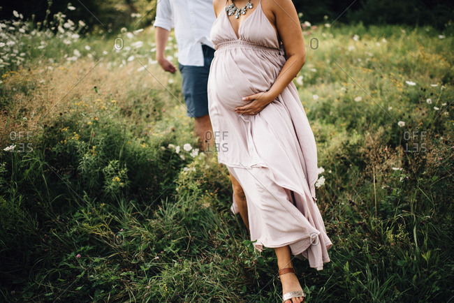 Maternity portrait of expecting couple walking through lush field
