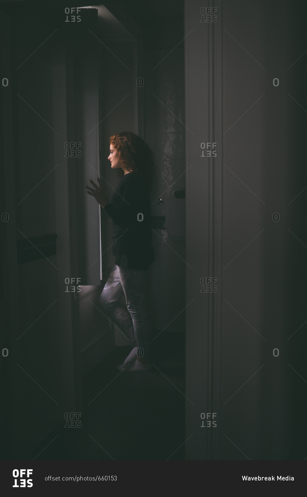 Thoughtful woman looking through window at home stock photo - OFFSET