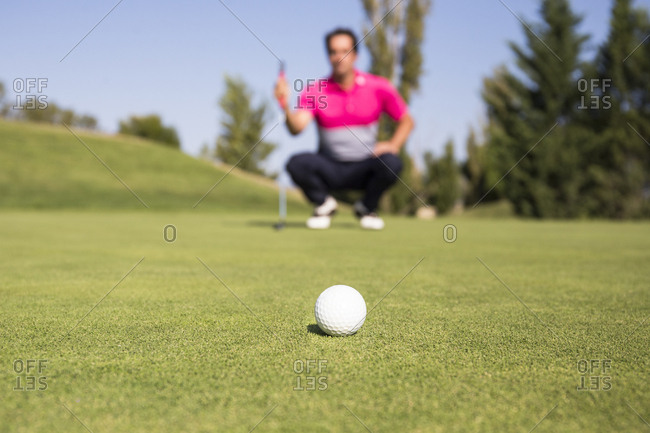 Low angle view of golfer crouching on green with ball in the foreground