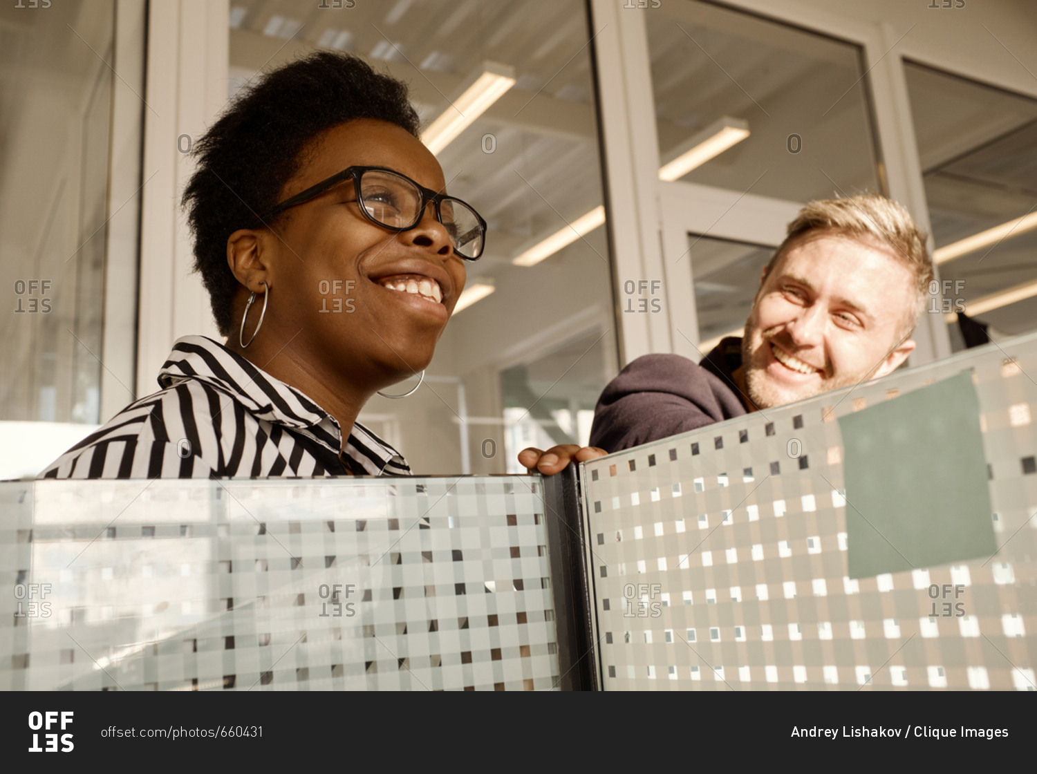 Attractive African American woman talking to her male colleague and smiling cheerfully in modern office with dividers, low angle view