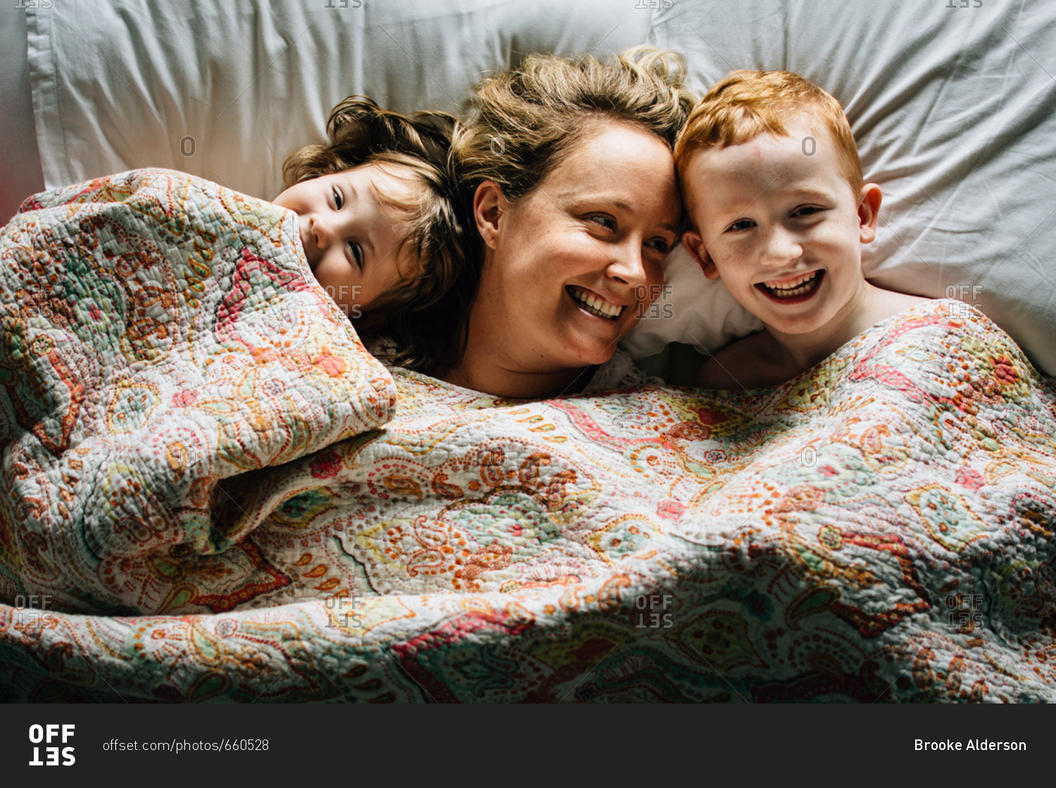 Mother and two kids cuddling in bed stock photo OFFSET