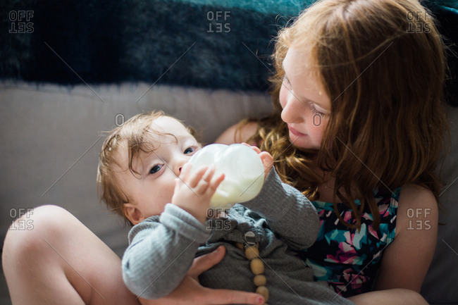 Older sister holding her baby sister while baby is drinking from a bottle