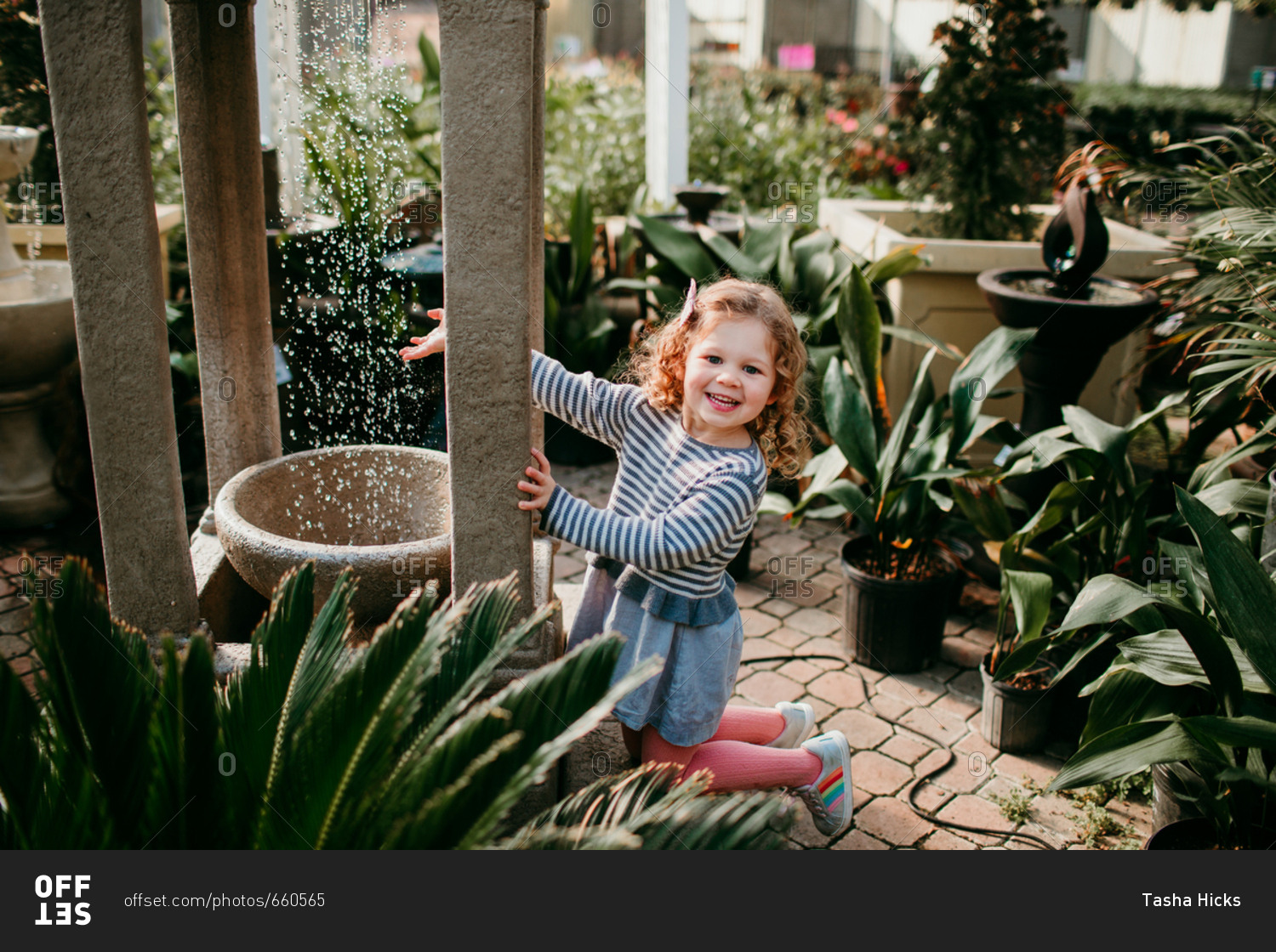 Little girl playing with water fountain in a garden center