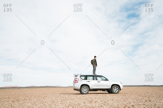 Side view of man standing on off-road vehicle at barren landscape against cloudy sky