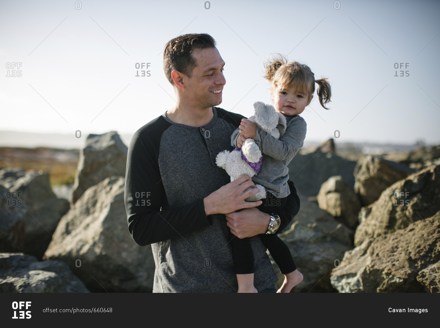 Portrait of cute daughter holding stuffed toy while being carried by father at beach