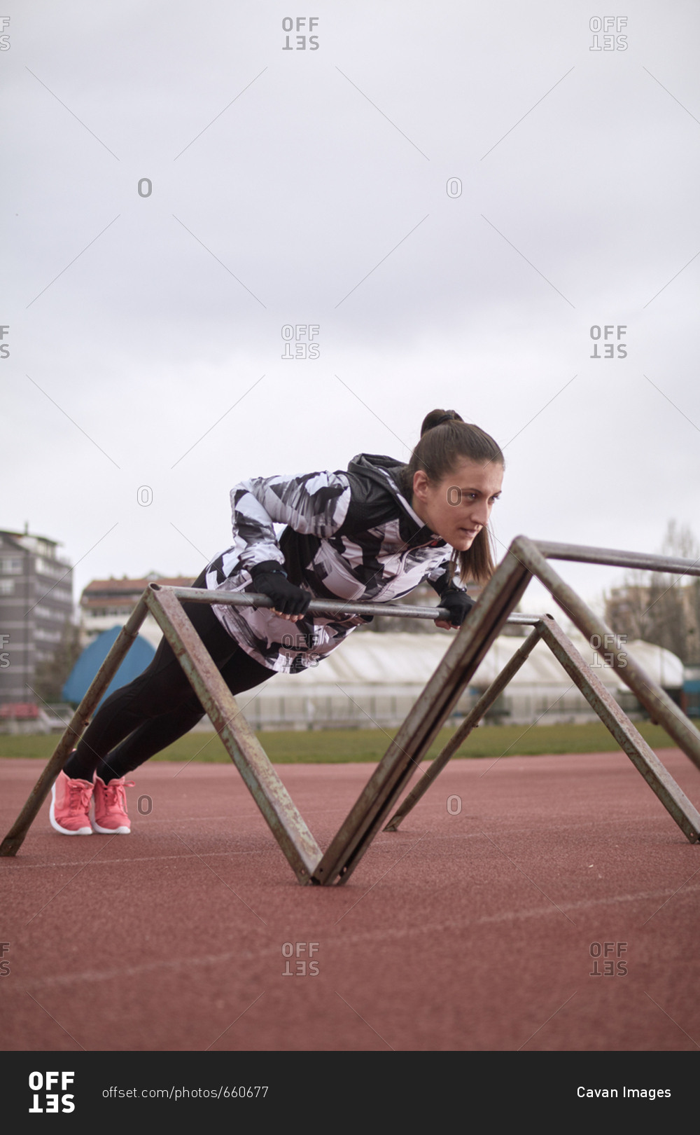 Female athlete exercising on gymnastics bars against sky at sports track