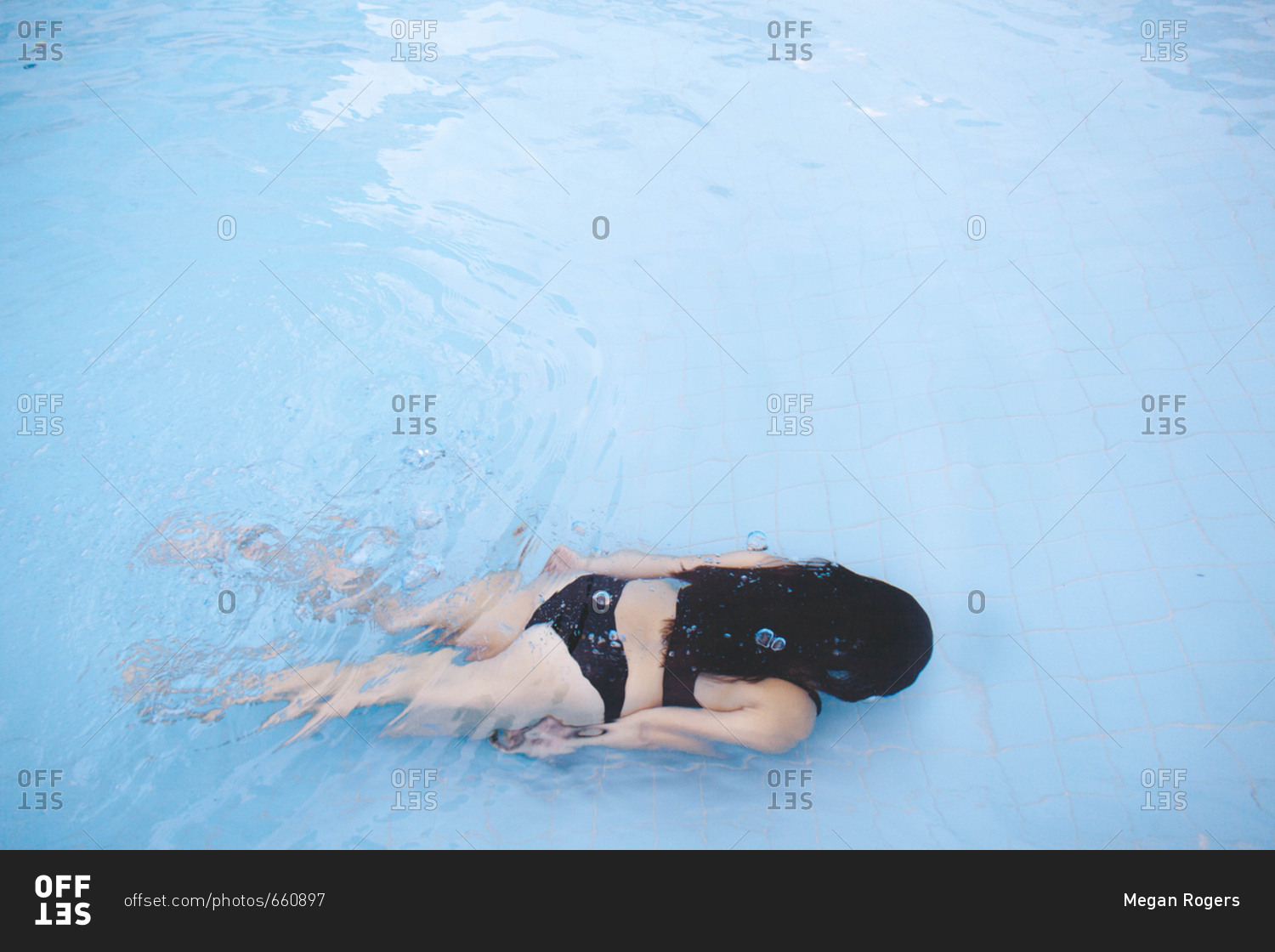 Dark haired woman in black bikini swimming underwater