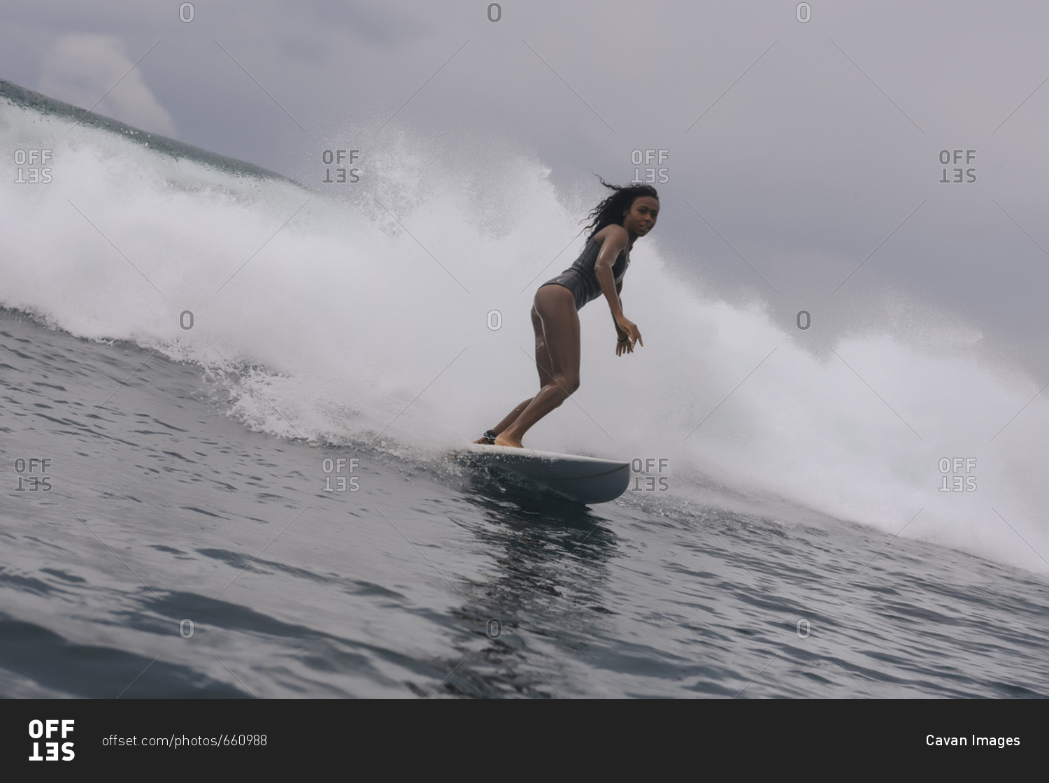 Side view of woman in wetsuit surfing on sea against cloudy sky