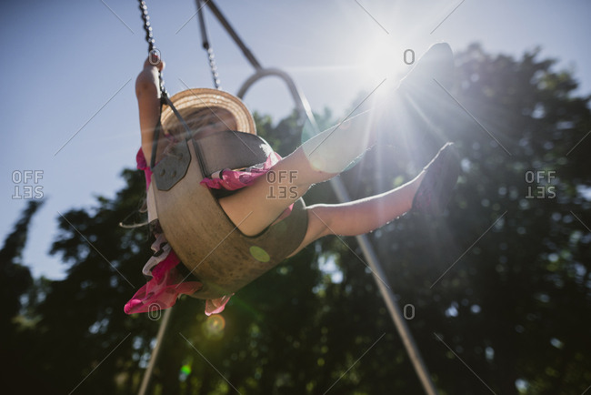 Low angle view of playful girl swinging on swing at playground during sunny day