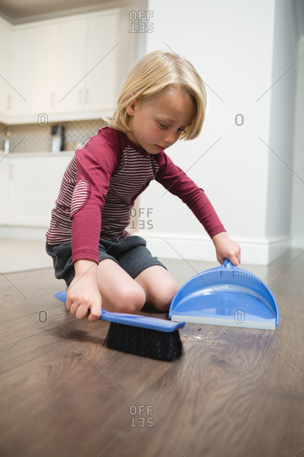 Boy sweeping dust with brush and dust pan at home