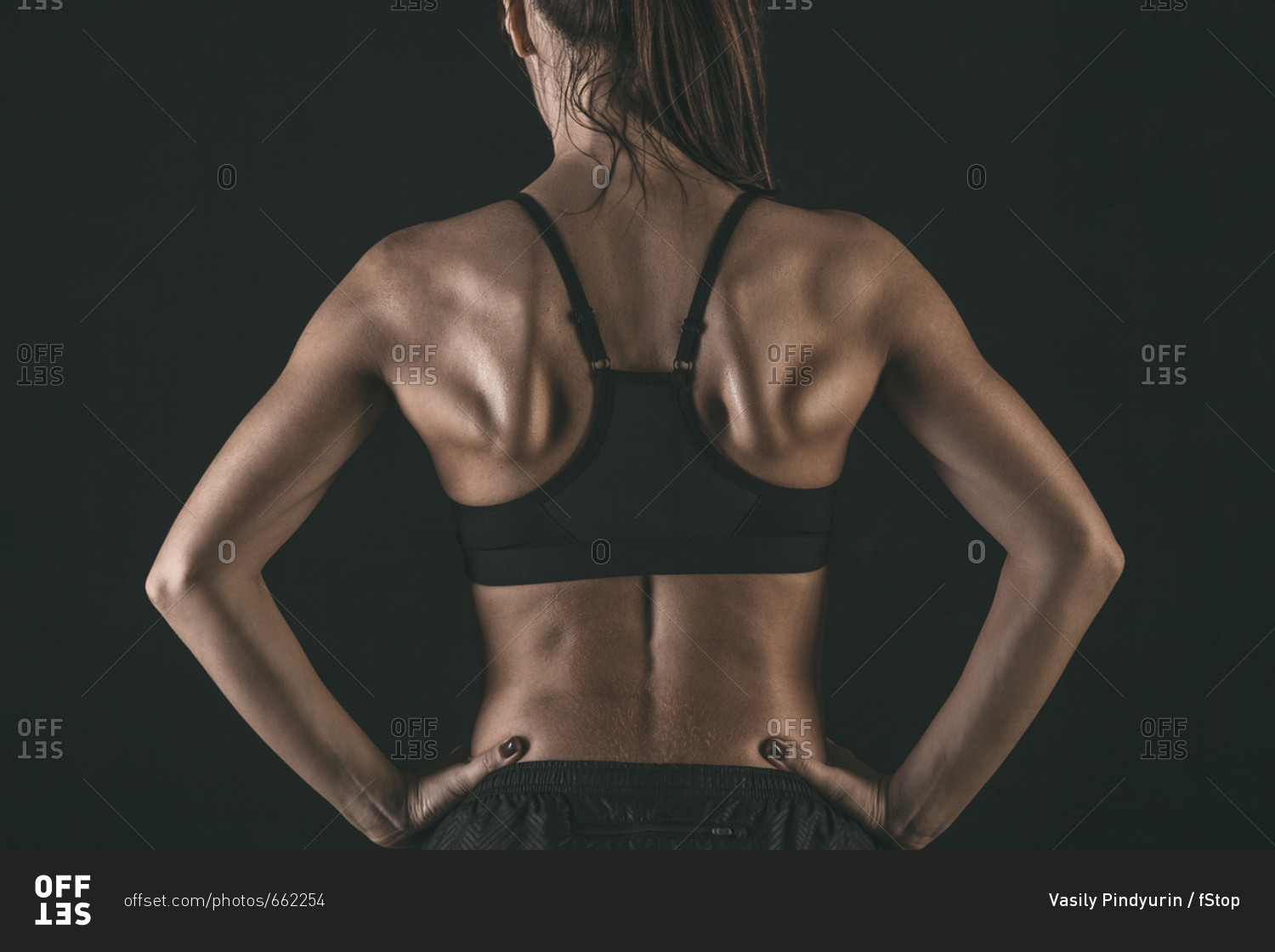 Rear view of female athlete wearing sports bra standing with hands on hip against black background