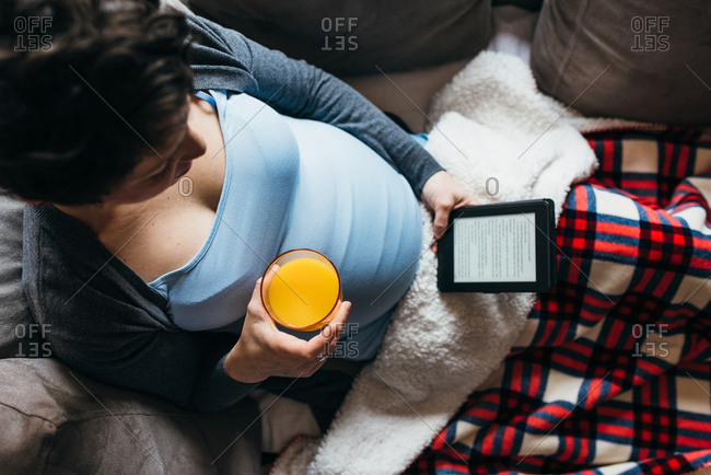 9 month pregnant woman relaxes in her bed reading a book on her tablet
