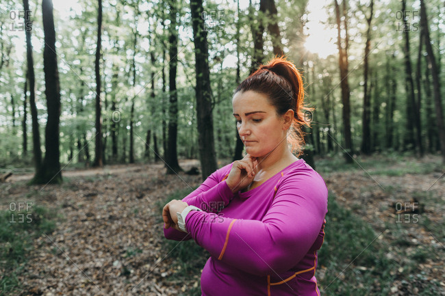 Portrait of a plus size female jogger measuring her pulse after a jog in a park