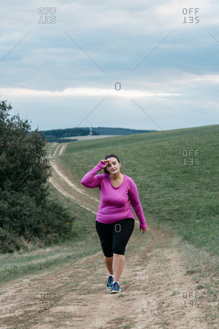 Tired voluptuous female jogger trying to catch her breath after a jog in a country