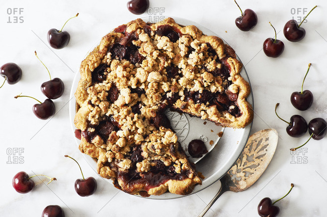 Overhead view of cherry crumb pie with pie server and  ripe cherries scattered around