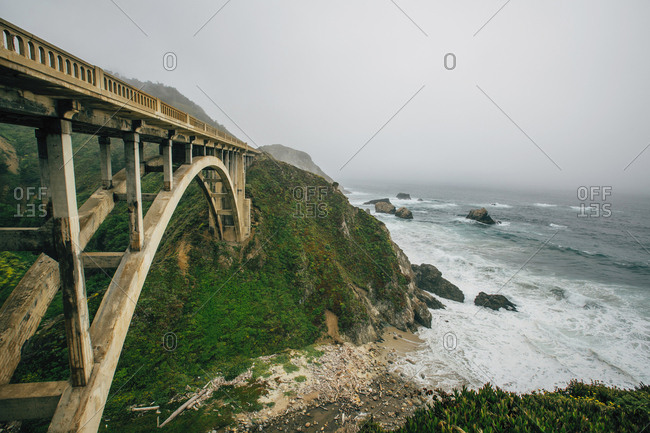 Bridge on mountain by sea against sky during foggy weather