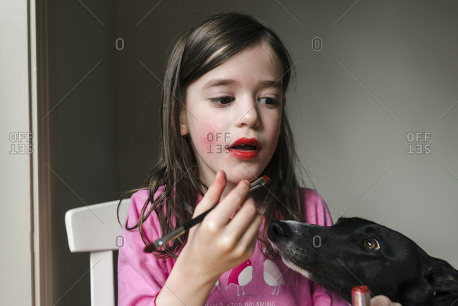 Young girl putting on lip stick as pet dog looks on