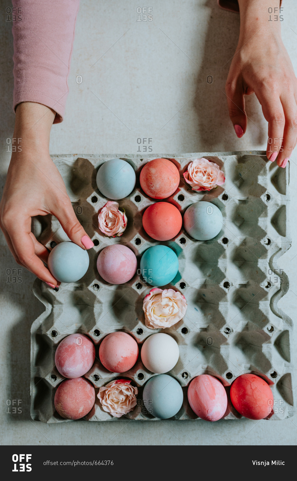 Person holding pastel Easter egg next to the other Easter eggs in carton