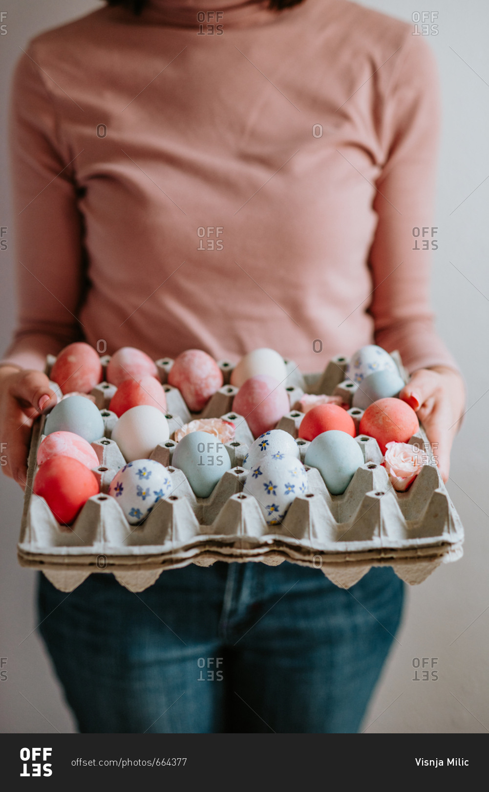 Woman wearing pastel colors holding carton of pastel Easter eggs
