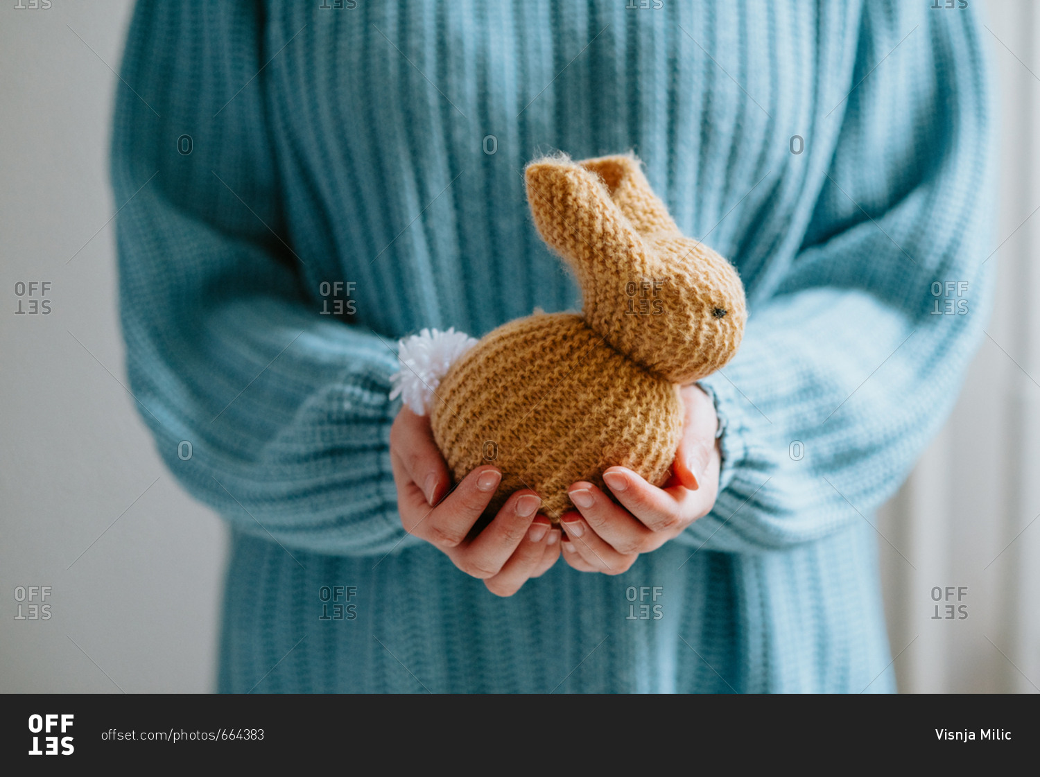 Person in pastel blue sweater holding cute knitted Easter bunny