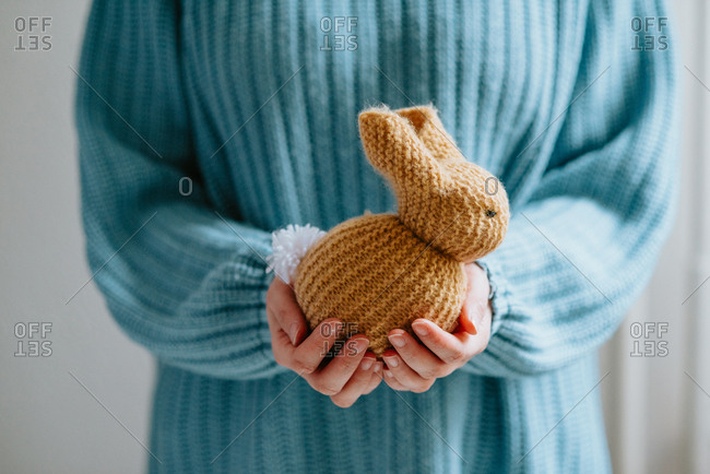 Person in pastel blue sweater holding cute knitted Easter bunny