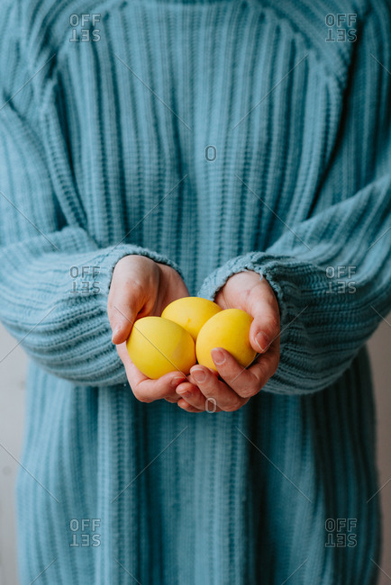 Person in pastel blue sweater holding three yellow Easter eggs