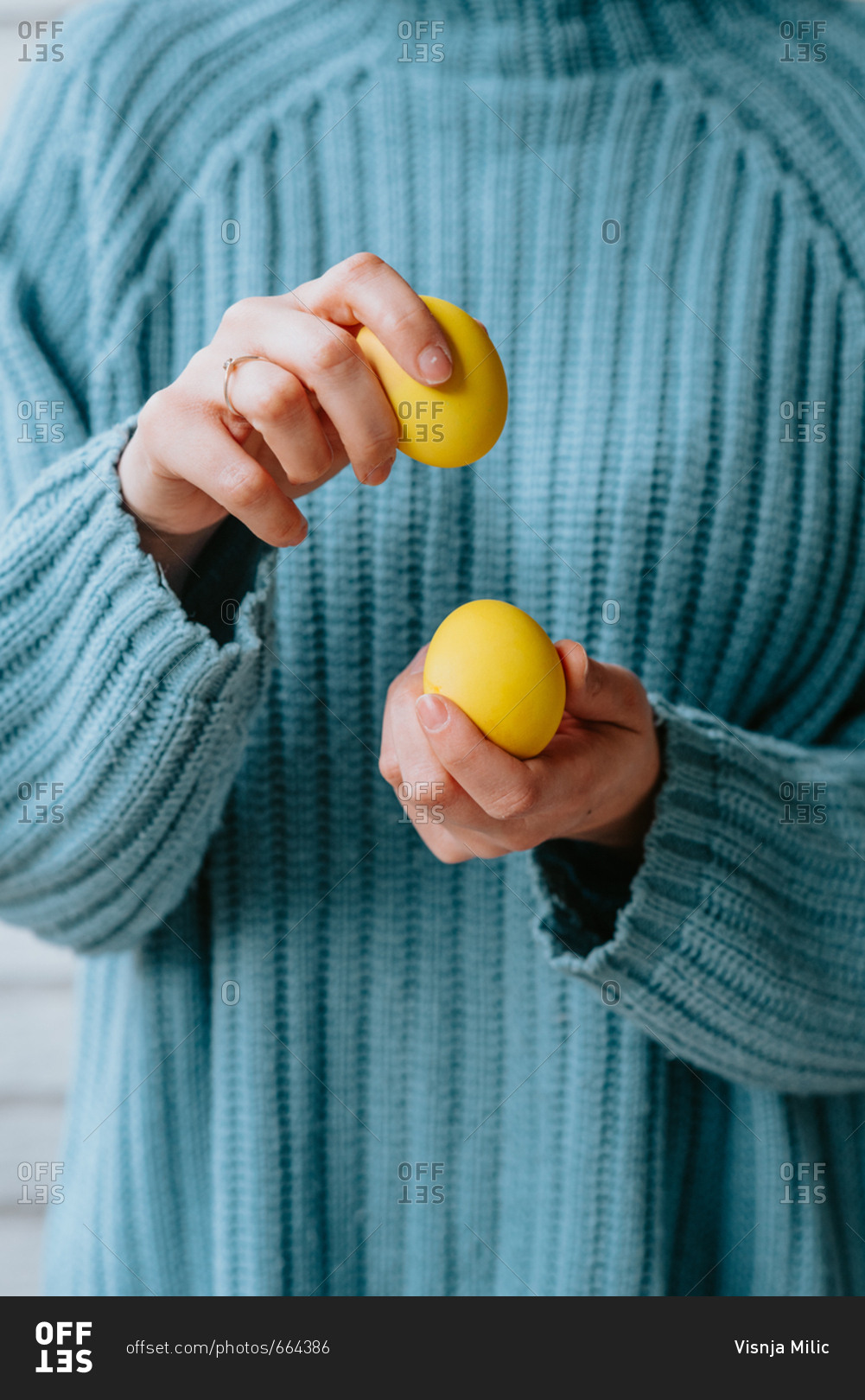 Person in pastel blue sweater holding three yellow Easter eggs