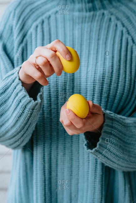 Person in pastel blue sweater holding three yellow Easter eggs